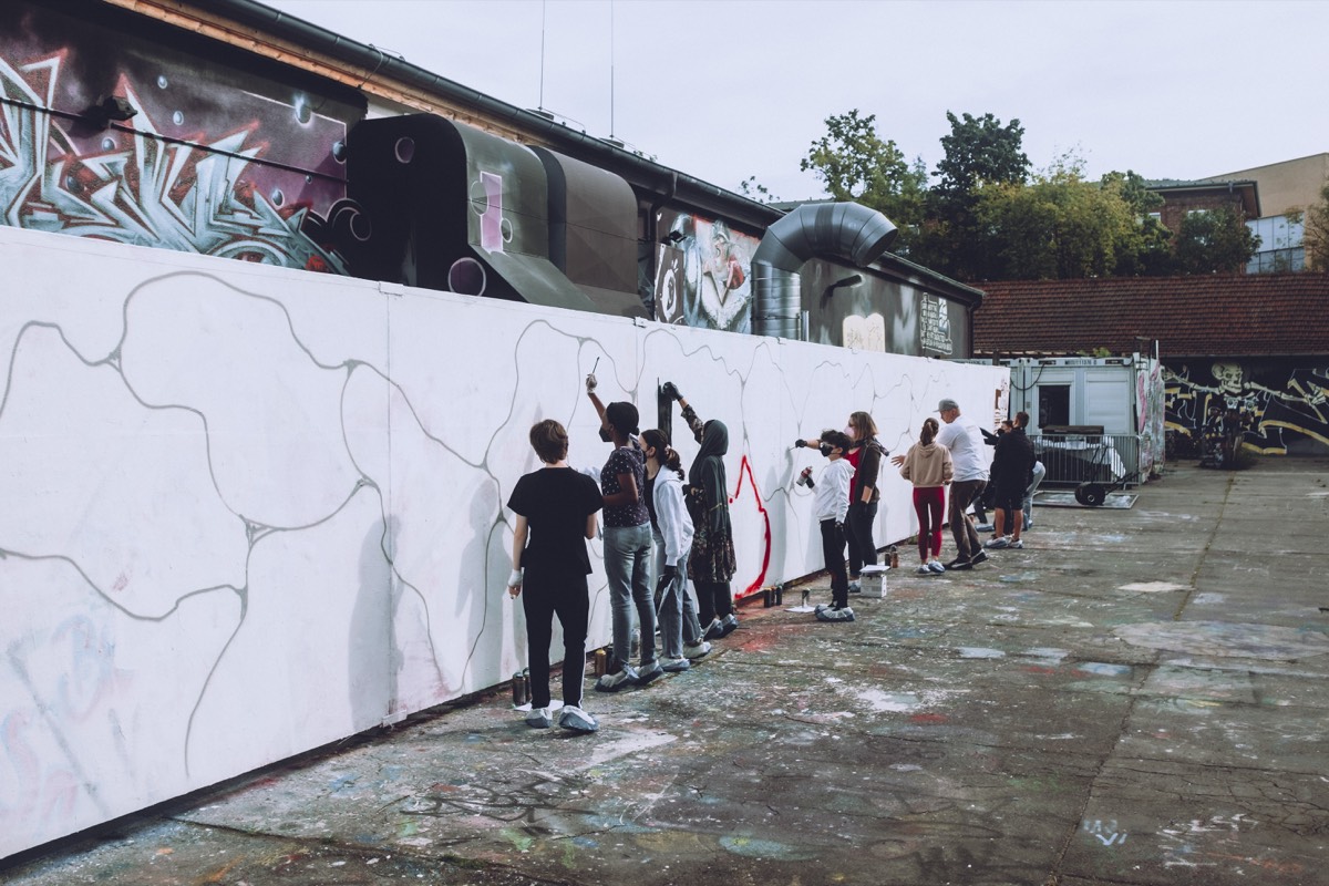 Schülerinnen und Schüler bemalen gemeinsam eine Wand im Rahmen eines Graffiti-Workshops